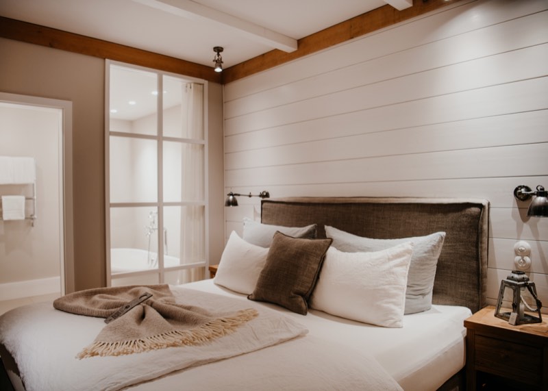 Hotelzimmer in Naturtönen mit Leinenkissen und Plaid, Glastür zum Bad mit Wanne