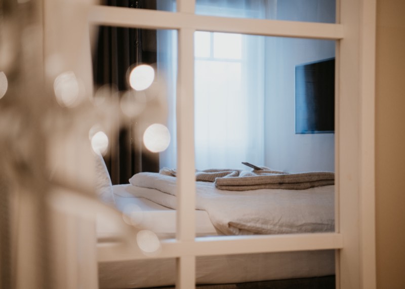 Blick durch eine weiße Sprossentür auf ein gemachtes Bett, Lichtpunkte im unscharfen Vordergrund