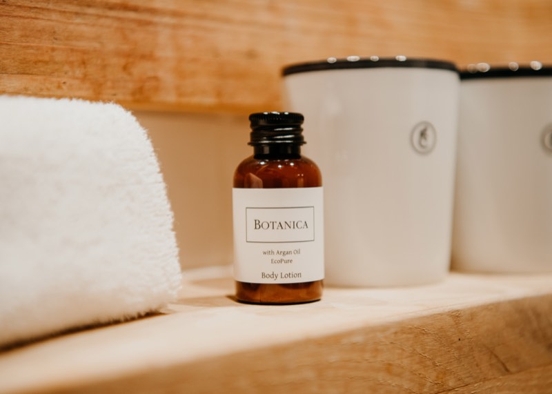 Fläschchen Body Lotion neben einem gerollten Handtuch auf einer Holzablage im Hotelbad