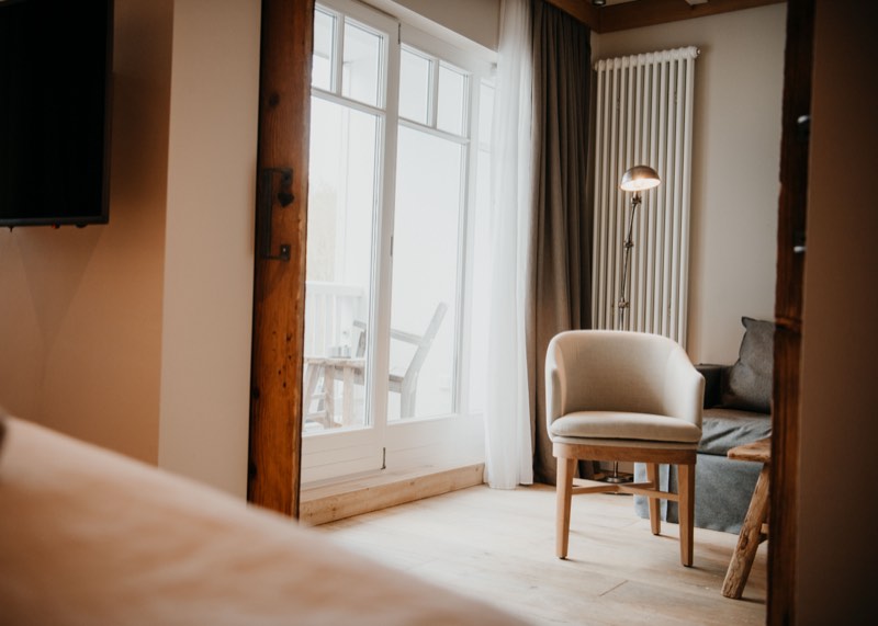 Hotelzimmer mit Polstersessel am Fenster, Stehlampe und Blick auf den Balkon