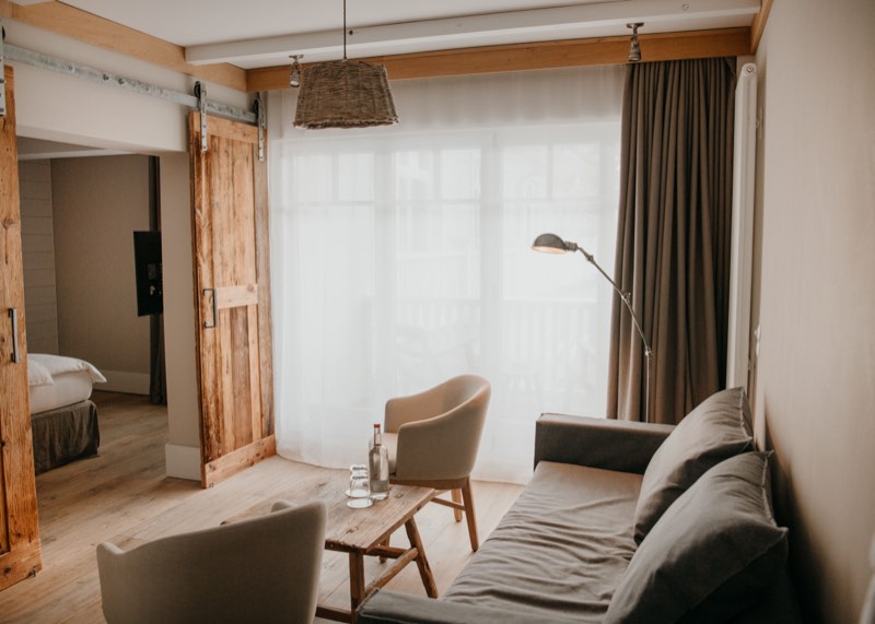 Wohnbereich einer Suite mit Sofa, Sesseln und Korbleuchte, Tageslicht hinter dem Vorhang