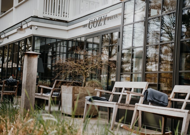 Terrasse mit Holzsesseln und Decken vor der Glasfassade eines Hotels, Gräser im Vordergrund
