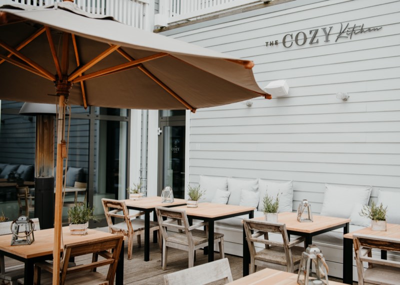 Restaurantterrasse mit Sonnenschirm, Holztischen und gepolsterter Bank an der Fassade
