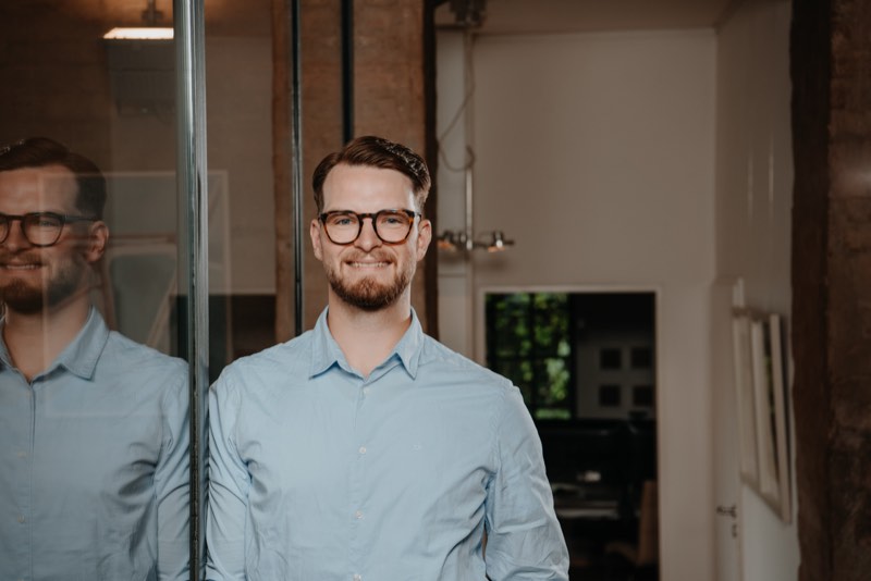 Businessporträt im Querformat, Mann mit Brille vor Glaswand und Backsteinpfeiler