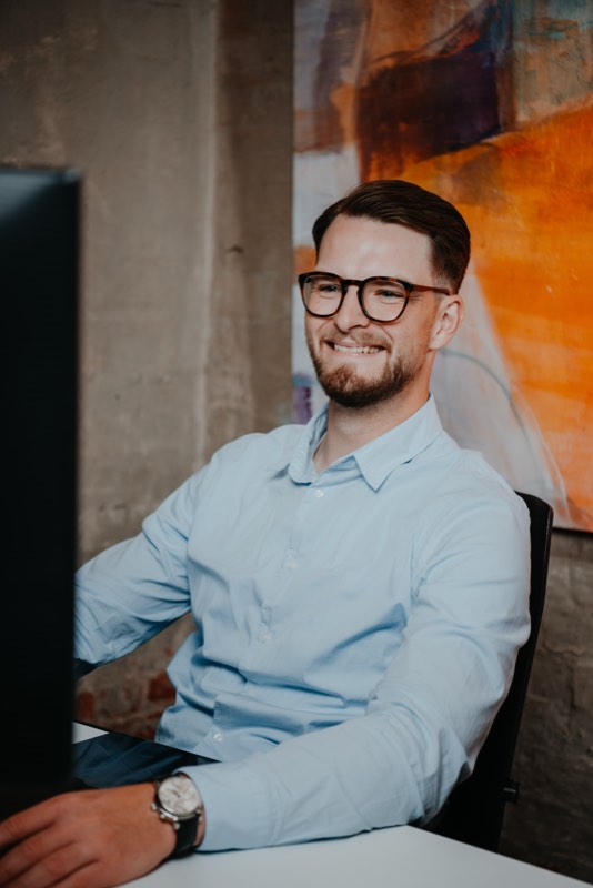Arbeitsplatz im Loft: Mann im hellblauen Hemd am Bildschirm, Betonwand und Kunst
