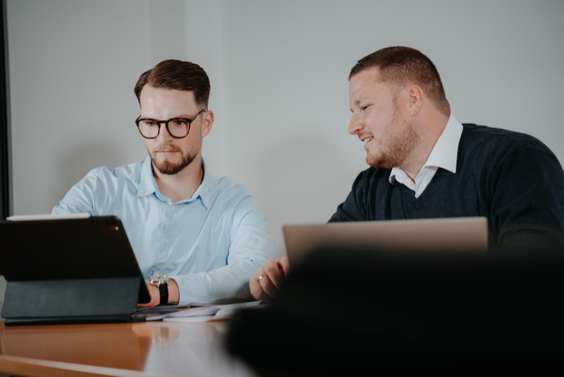 Zwei Männer am Besprechungstisch mit Tablet und Laptop, konzentrierte Arbeit
