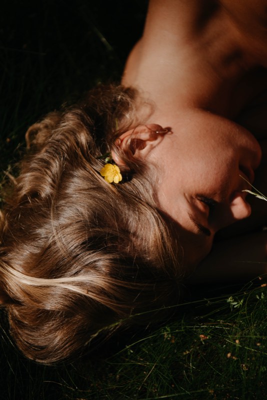 Nahaufnahme: blondes Haar mit gelber Blüte, das Gesicht ruht im Gras