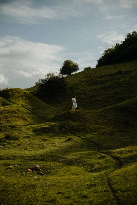 Schwangere steht auf einer Kuppe im Hügelland, darüber ziehende Wolken
